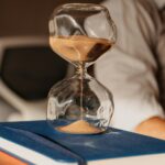 A glass hourglass with sand on books in a modern office environment.